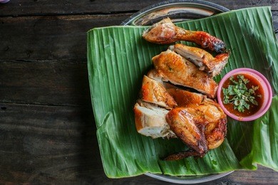 grilled chicken with chili sauce on banana leaf and wooden background -  thai traditional menu