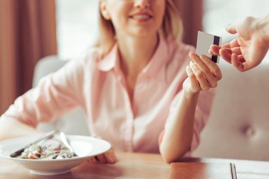 beautiful young business woman is paying with a credit card for business lunch at the restaurant, close-up