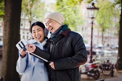 couple laughing at their pictures taken on smartphone against canal in amsterdam