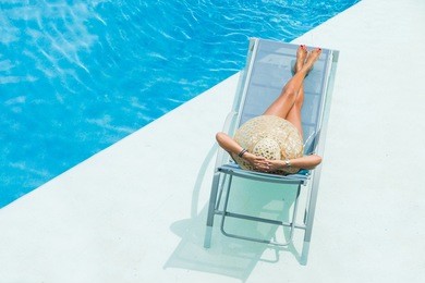 woman with hat  enjoying on sunbed at swimming pool