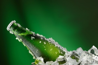 cold green bottle of beer with water droplets and ice cubes over green background
