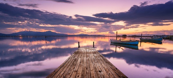 perspective view of a wooden pier in the lagoon at sunset with fisherman boats, and a lot of reflections on the water.