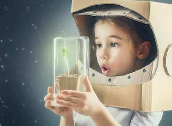 child is dressed in an astronaut costume. child sees a sprout in a glass case. the concept of environmental protection.