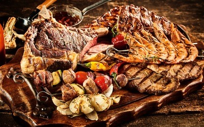 various types of barbecued beef and seafood with roasted tomatoes and potatoes over wooden table background