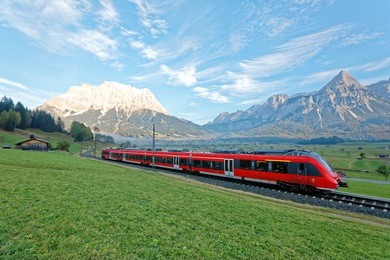 panoramic view of a train traveling on green fields with mountain zugspitze in background on a beautiful sunny day in lermoos, tirol, austria ~ beautiful summer scenery of idyllic tyrolean countryside