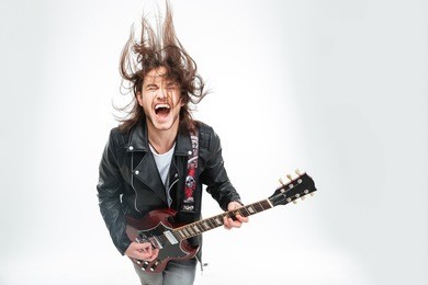 excited young man in black leather jacket with electric guitar shouting and shaking head over white background