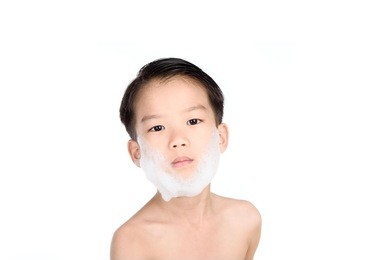 young boy put foam on his face before shaving in the bathroom.