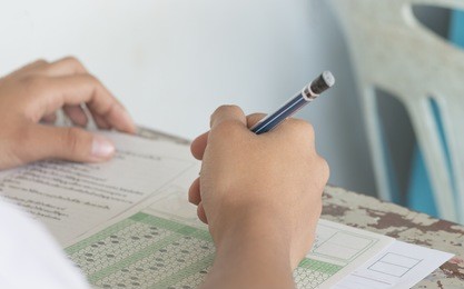 asian students holding pencil in hand doing multiple-choice quizzes or testing exams answer sheets exercises on old wood table in secondary school, college university classroom in education concept