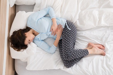 young woman with stomach ache lying on bed