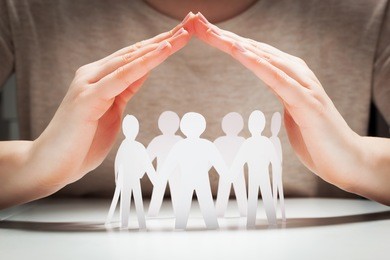 paper people under hands in gesture of protection. concept of insurance, social protection and support. 