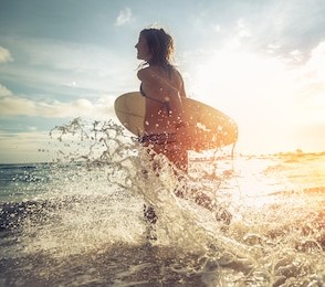 woman running into the sea with surf board