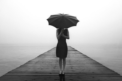woman with umbrella contemplates peacefully in front of a mysterious lake