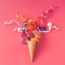 ice cream cone with colorful party streamers on pink background. flat lay