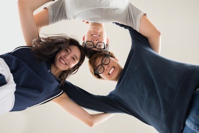 hugging asian friends standing in circle and smiling ta camera, view from below