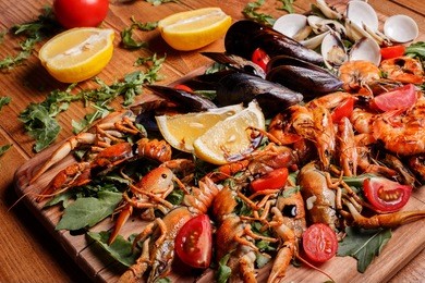 fresh mussels, crayfish, shrimp decorated with arugula, tomatoes, lemon and sauce on a wooden board. seafood platter