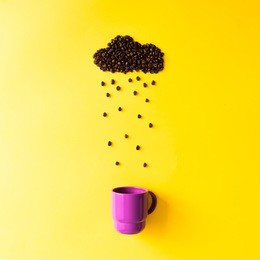 coffee beans in shape of rainy cloud with purple cup on yellow background. weather concept.