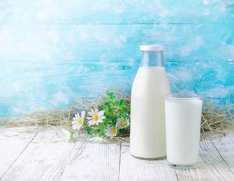a bottle and glass of milk on a wooden table on blue background