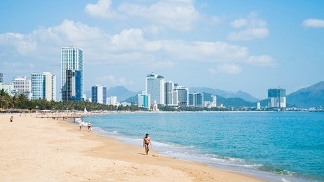 people walking on beach in ocean's bay by background of the city and mountains. shot in nha trang, vietnam.