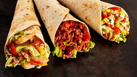 close up still life trio of tex mex fajita wraps on dark background - variety of gourmet grilled flour wraps stuffed with shrimp, chili and chicken and fresh vegetables - with copy space