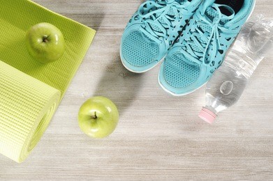 yoga mat with sport shoes and healthy food on a wooden background