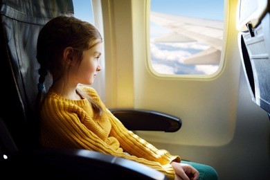 adorable little girl traveling by an airplane. child sitting by aircraft window and looking outside.