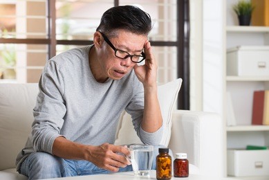 portrait of mature asian man having headache, sitting on sofa at home

