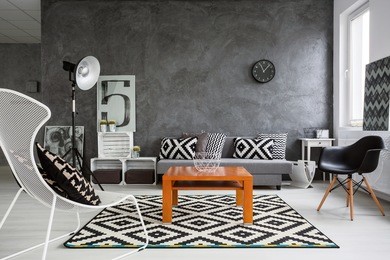 trendy, grey living room with sofa, chairs, standing lamp, wood coffee-table and pattern decorations in black and white 