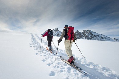two elderly alpine skiers climb on skis and sealskins