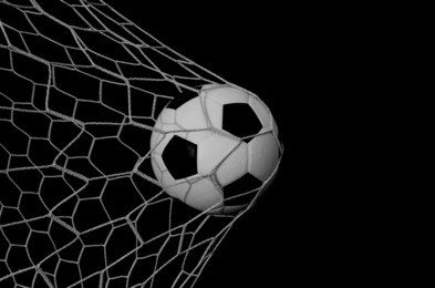 soccer football in goal net with green grass field.