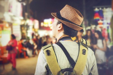 young male backpacker walking in a famous street night market in asia (grainy vintage tone and soft focus)