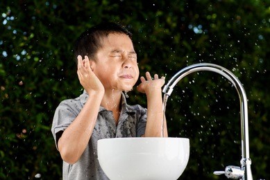 young asian boy washing his face by water from the brand new faucet.