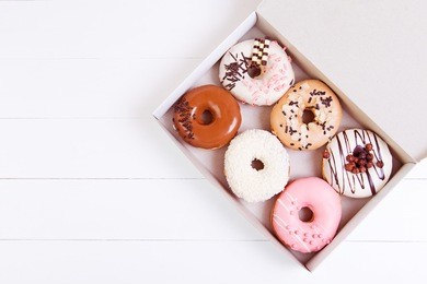 colored delicious donuts with sprinkles in a box on a white wooden background