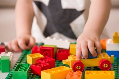 close up of child's hands playing with colorful plastic bricks at the table. toddler having fun and building out of bright constructor bricks. early learning.  stripe background. developing toys