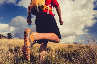 hiking man or trail runner walking in mountain inspirational landscape. fitness lifestyle hiker trekker walk in grass, fall autumn nature. travel in italy, europe. selective focus on a sports shoe. 