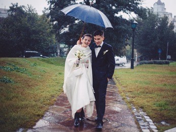 the romantic walking of newlyweds. the groom and bride are walking under umbrella in the rain in the park.
they are happy. newlyweds in love. tis is their wedding day. 