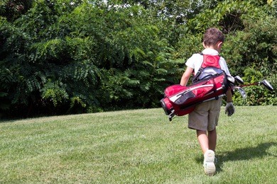 little boy golfer walking with his golf bag on the fairway