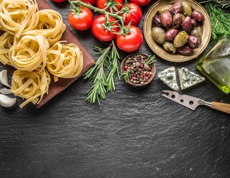 pasta ingredients. cherry-tomatoes, spaghetti pasta, rosemary and spices on a graphite board.