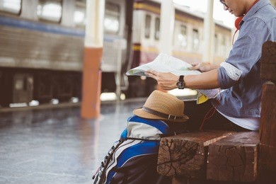 man sitting with map. travel bag at the train station.vintage filter effected .