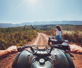 young people on quad bikes on a countryside trail. view from a quad bike with woman driving an atv in front on a sunny day.