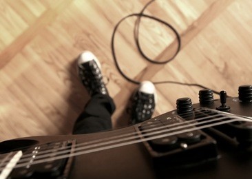 playing electric guitar. first person perspective: guitar, sneakers, cord.