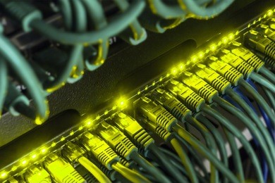  close up of green network cables from data center connected with patch cord to black switch glowing in the dark. blurred frame vignetting 