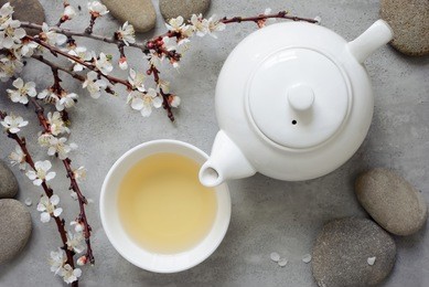 tea concept, cup with tea and white teapot decorated with blooming spring tree branch, top view
