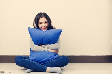 young asian woman sitting and hugging blue pillow with smiley face.