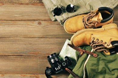travel accessories set on wooden background: old hiking leather boots, pants, backpack, map, vintage film camera and sunglasses. top view point.