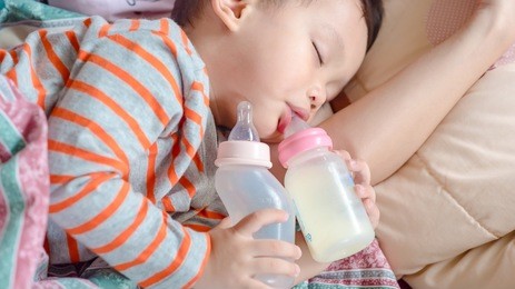   milk bottle and water bottle holding by asian  boy.the kids sleeping in mother arm 