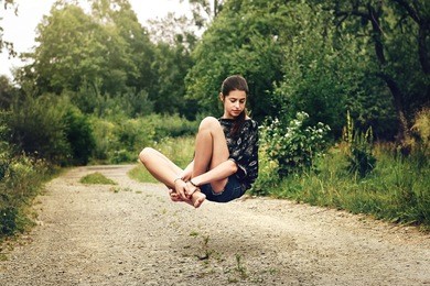 beautiful stylish hipster girl levitating with peaceful feelings on the road near woods in summer