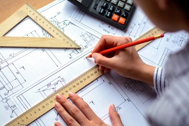 girl architect draws a plan, graph, design, geometric shapes by pencil on large sheet of paper at office desk. soft focus