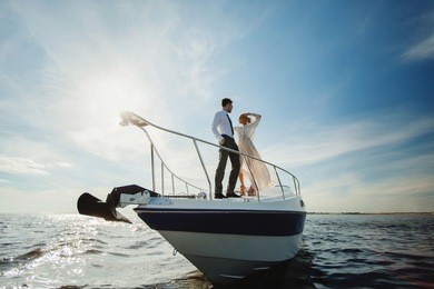fashionable stylish standing young couple posing on luxury motorboat yacht on blue sky with clouds and sea landscape background in daylight view from the water