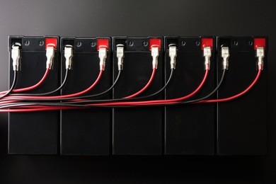 rechargeable batteries, and electrical wires. industrial battery hooked up in parallel with long red and black cable bundles, coming from the terminal. 