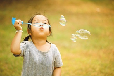 a little asian girl blowing soap bubbles, closeup portrait beautiful curly baby